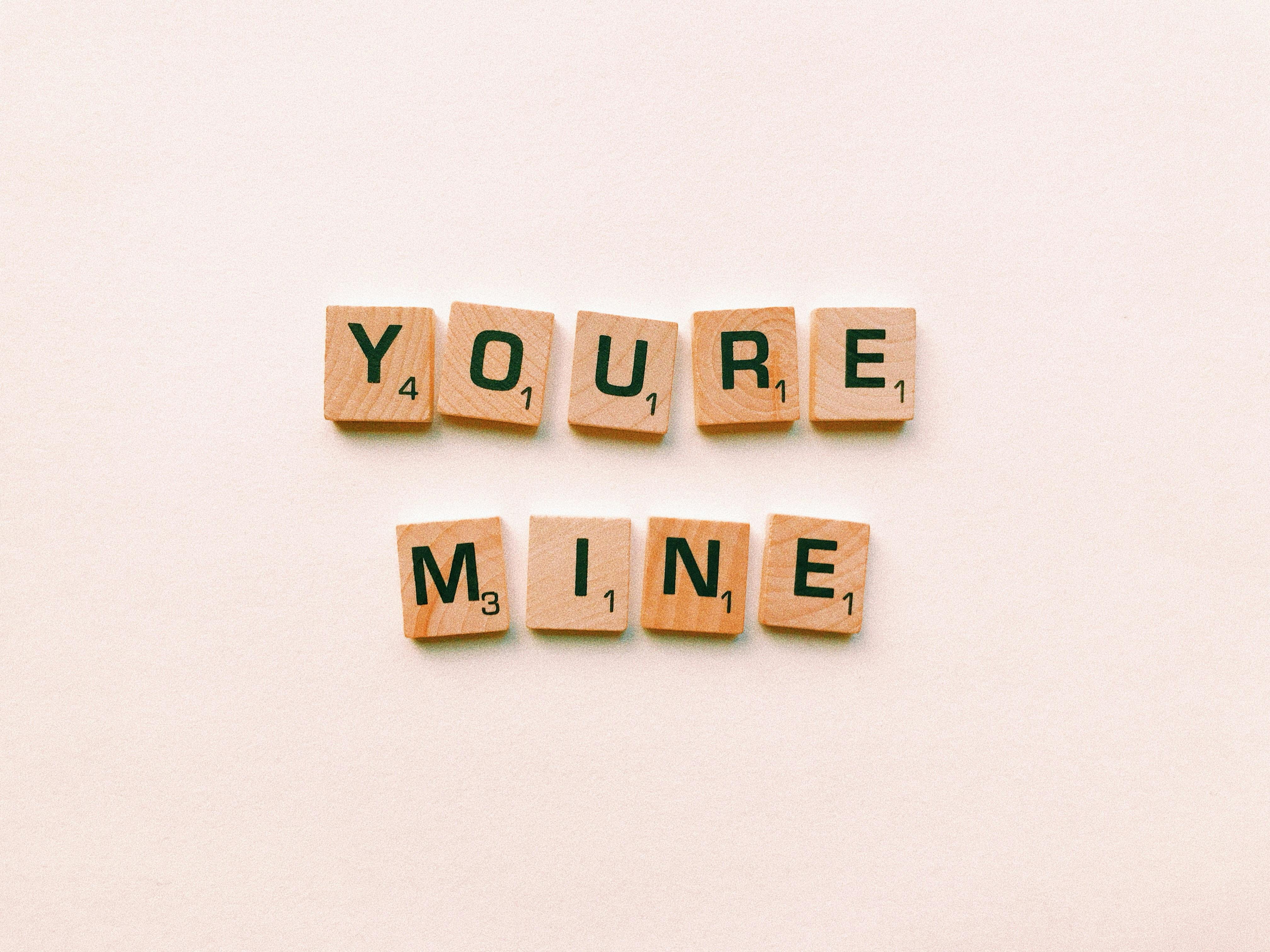 Romantic message You're Mine created with wooden Scrabble tiles on a pink background.