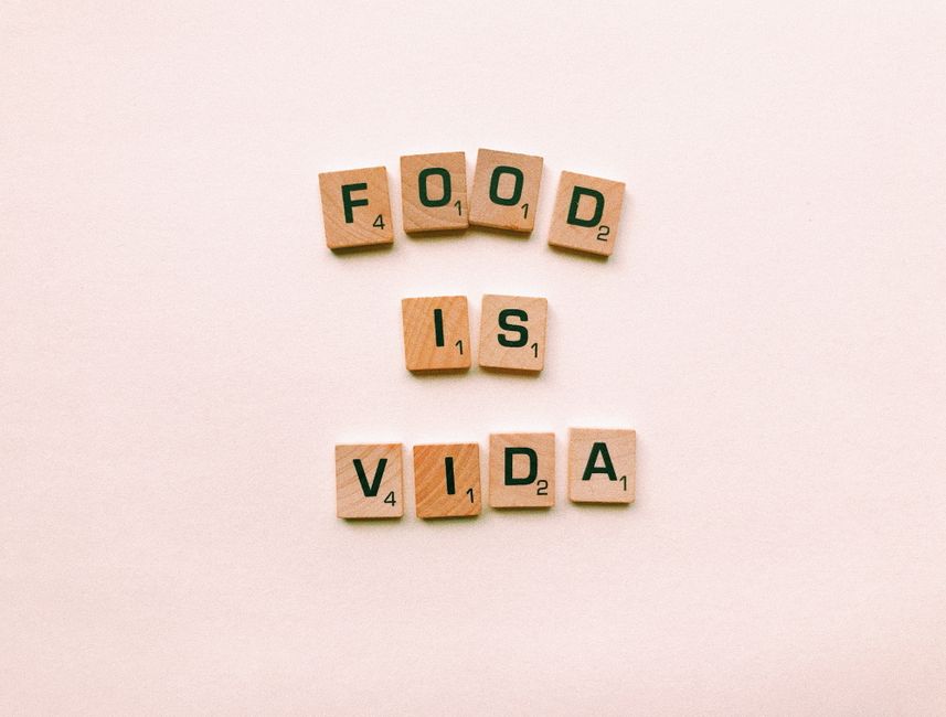 Como Criar um Estilo de Vida Sustentável e Aconchegante 2 Wooden letter tiles spell 'FOOD IS VIDA' on a soft pink background.