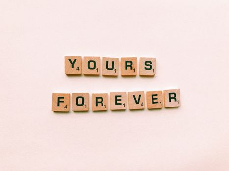 Scrabble tiles spelling 'Yours Forever' on a pink background, symbolizing lasting love.