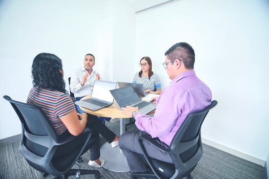 Diverse team engaged in a corporate meeting with laptops in a bright, modern office setting.