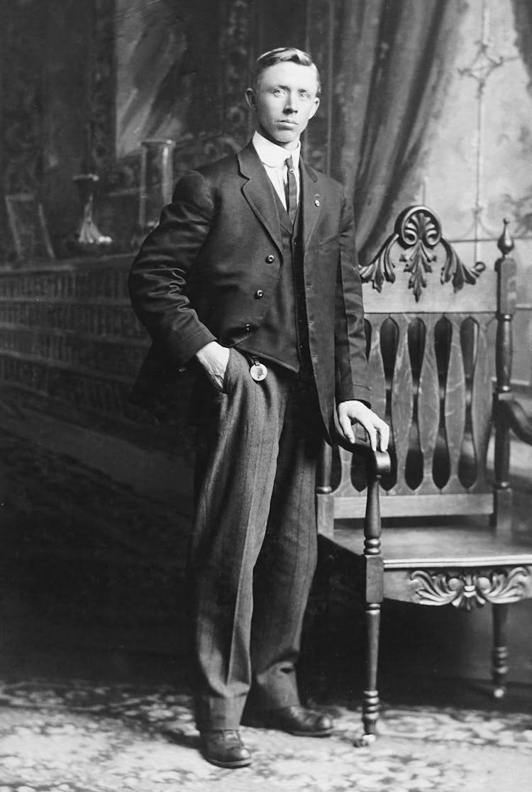 Man In Suit Standing Beside Armchair