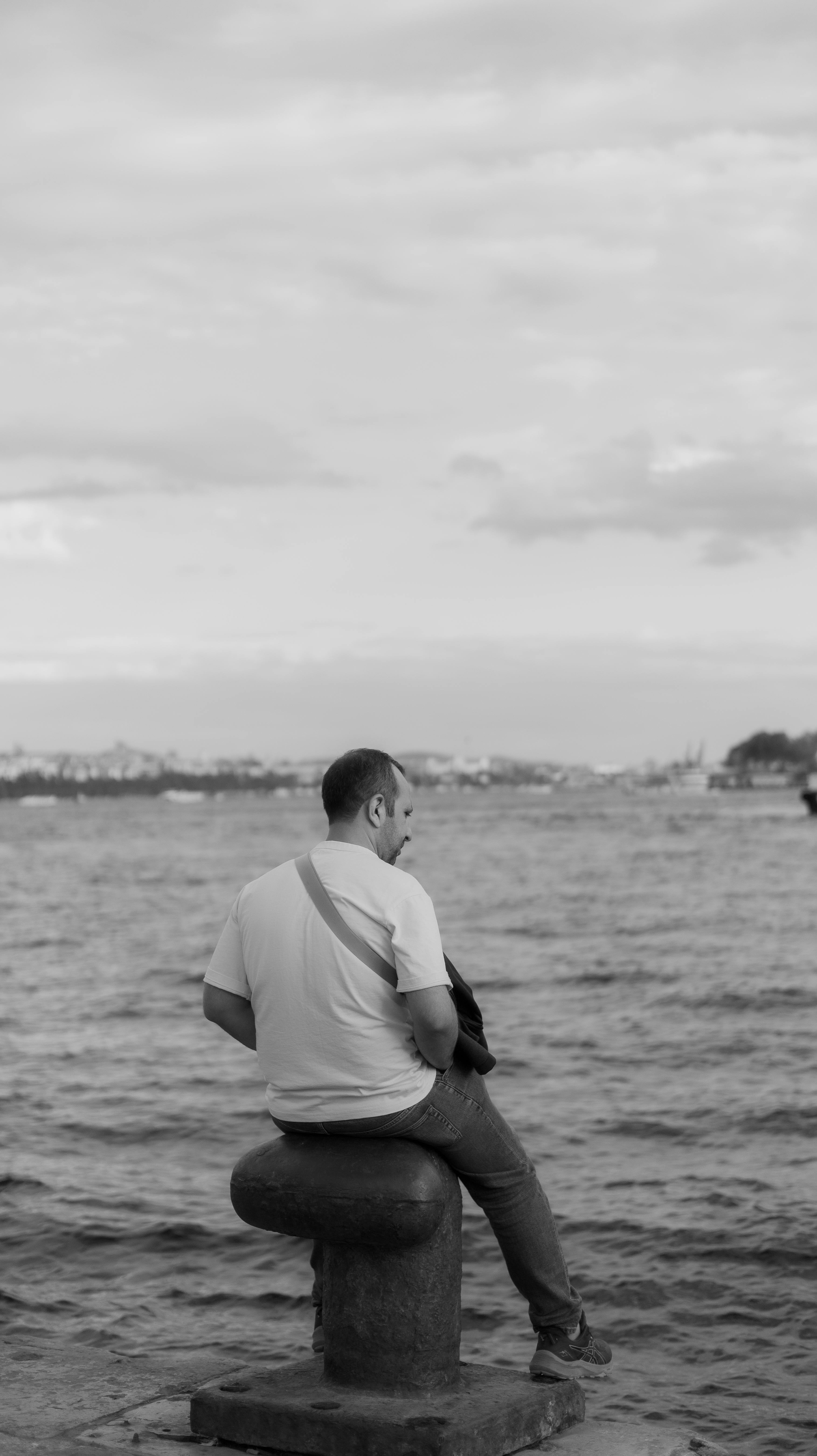 在土耳其伊斯坦布尔的博斯普鲁斯海峡旁，一名男子若有所思地坐在那里，他的照片黑白相间