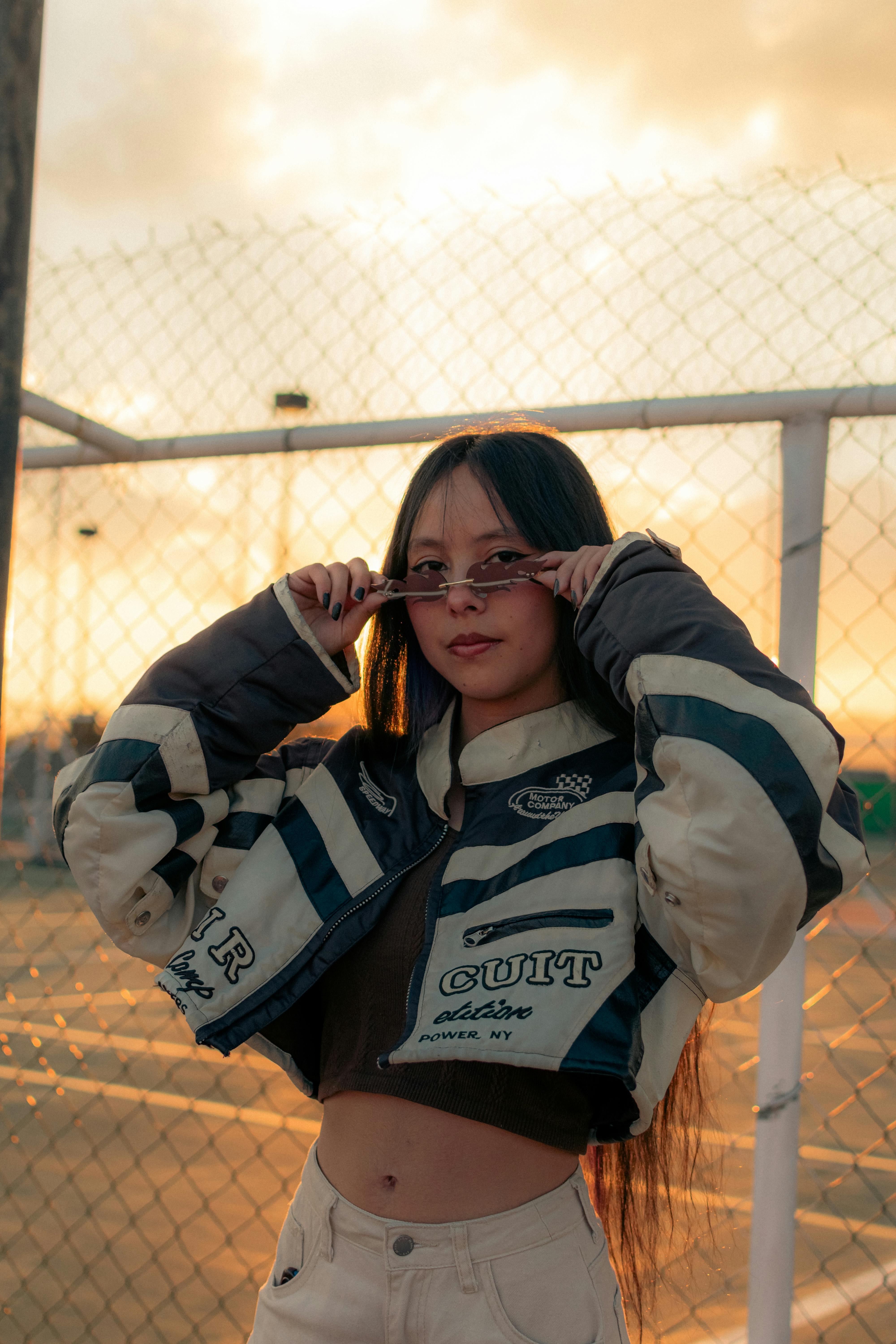 十几岁的女孩穿着时髦的夹克和太阳镜，在日落的背景下