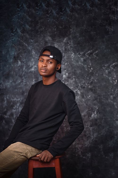 Free Young man in casual attire leaning on stool against textured backdrop in studio. Stock Photo