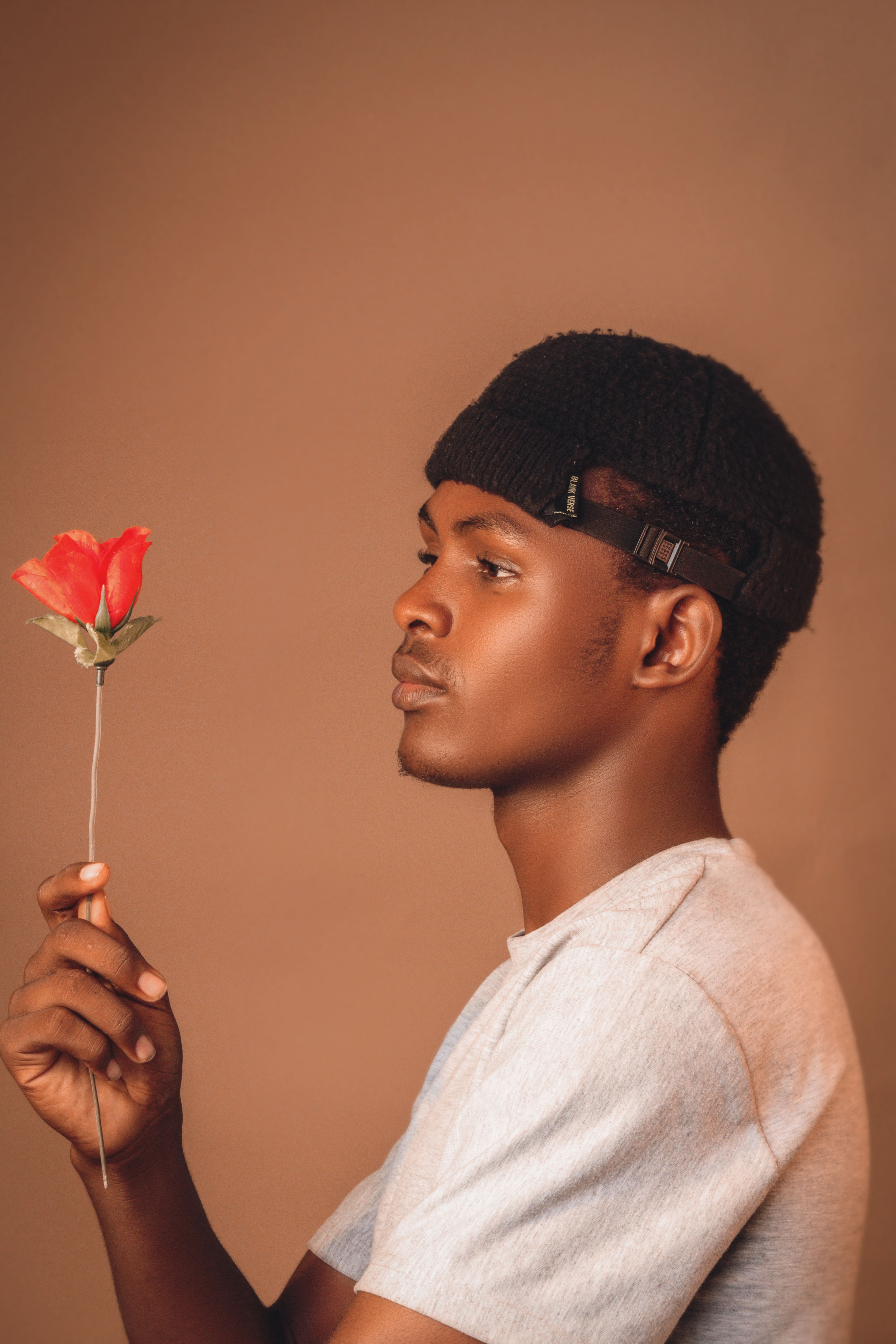 Side profile of a man holding a red flower against a brown background, evoking thoughtfulness.