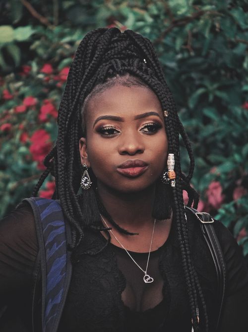 Free Elegant portrait of a young African woman with braided hair, wearing jewelry, set outdoors against a natural background. Stock Photo