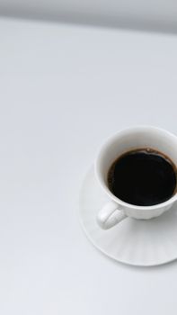 A minimalist photo of a white cup filled with black coffee on a white table.