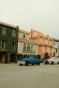 Charming San Francisco street with vintage and modern cars parked in front of colorful homes.