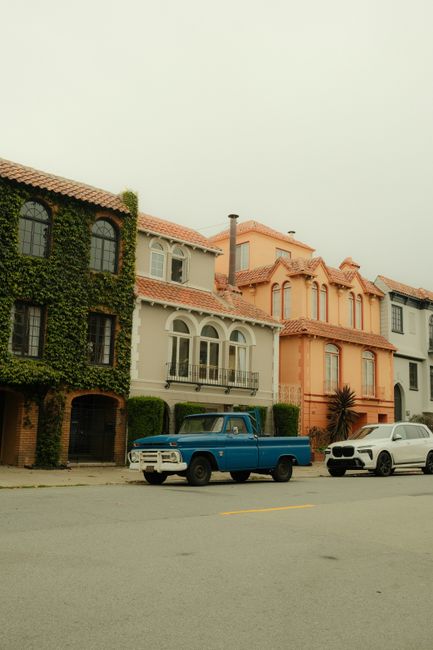 Charming San Francisco street with vintage and modern cars parked in front of colorful homes.