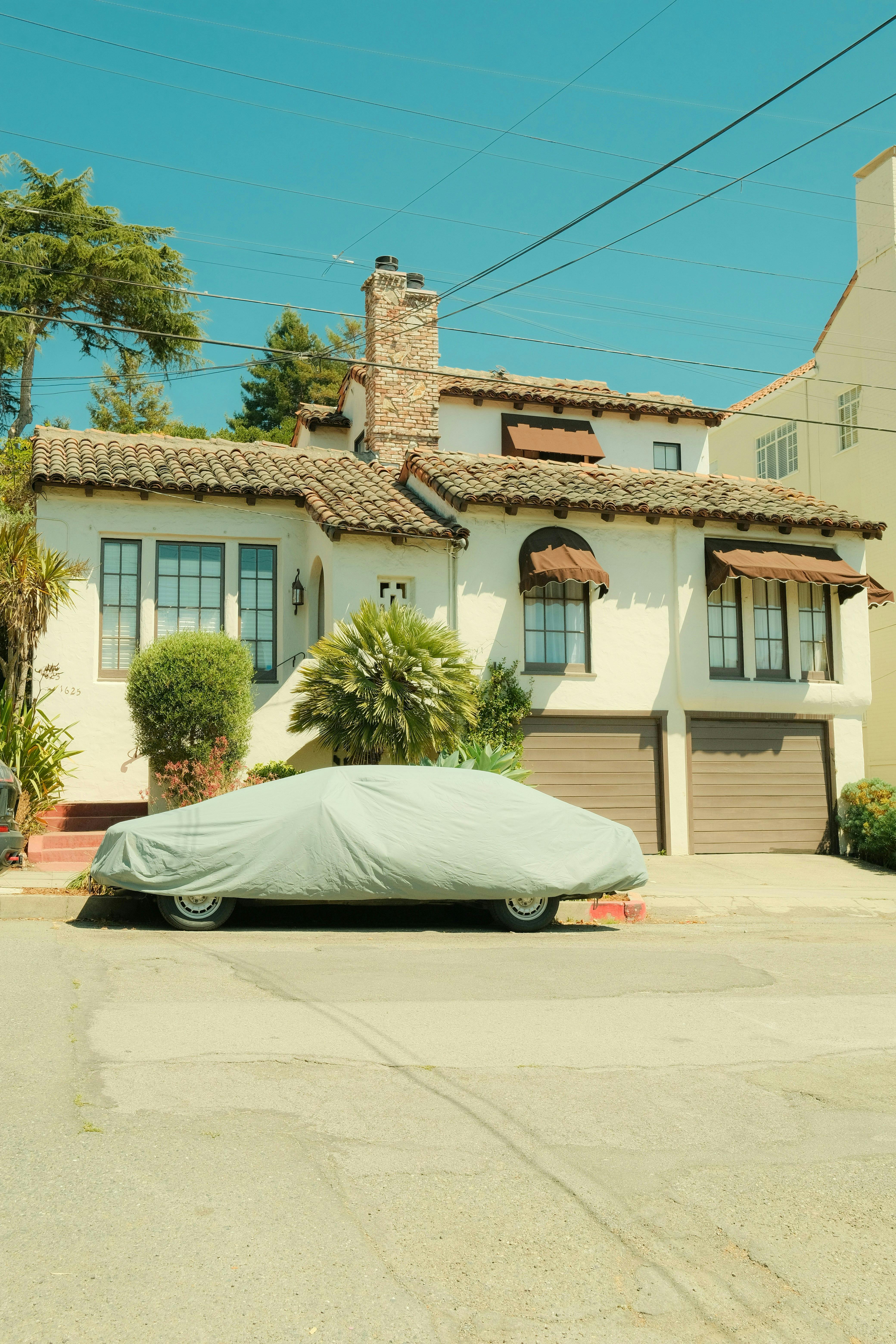 Vintage Mediterranean house with car covered in the driveway under a bright sky.