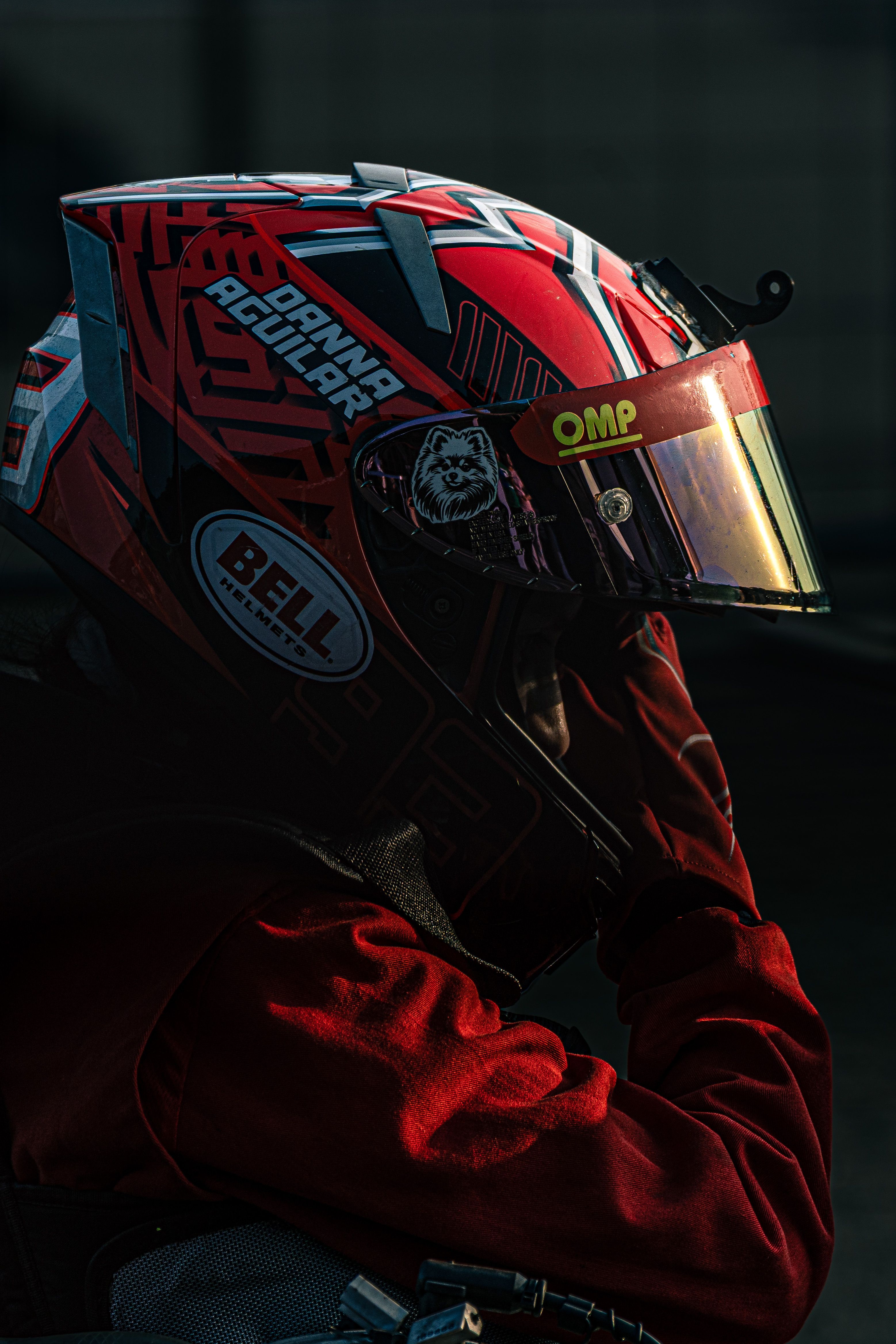 Close-up of a racer wearing a vibrant red helmet with visor reflecting ambient light.