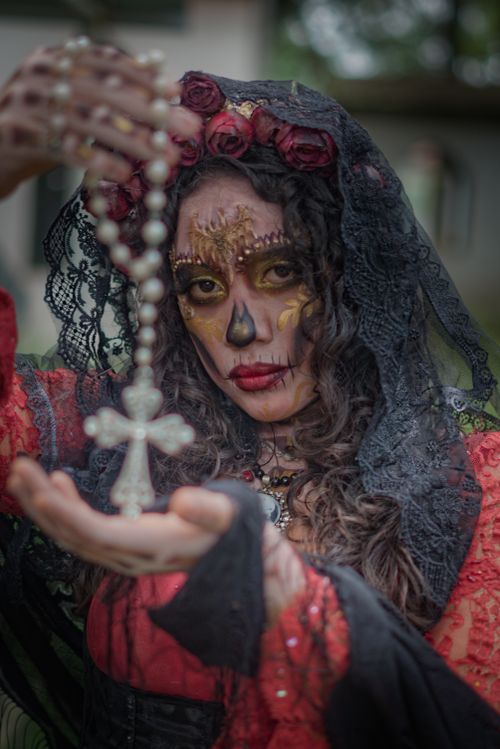 Free Woman in Day of the Dead makeup with cross necklace in hand, vibrant and artistic. Stock Photo