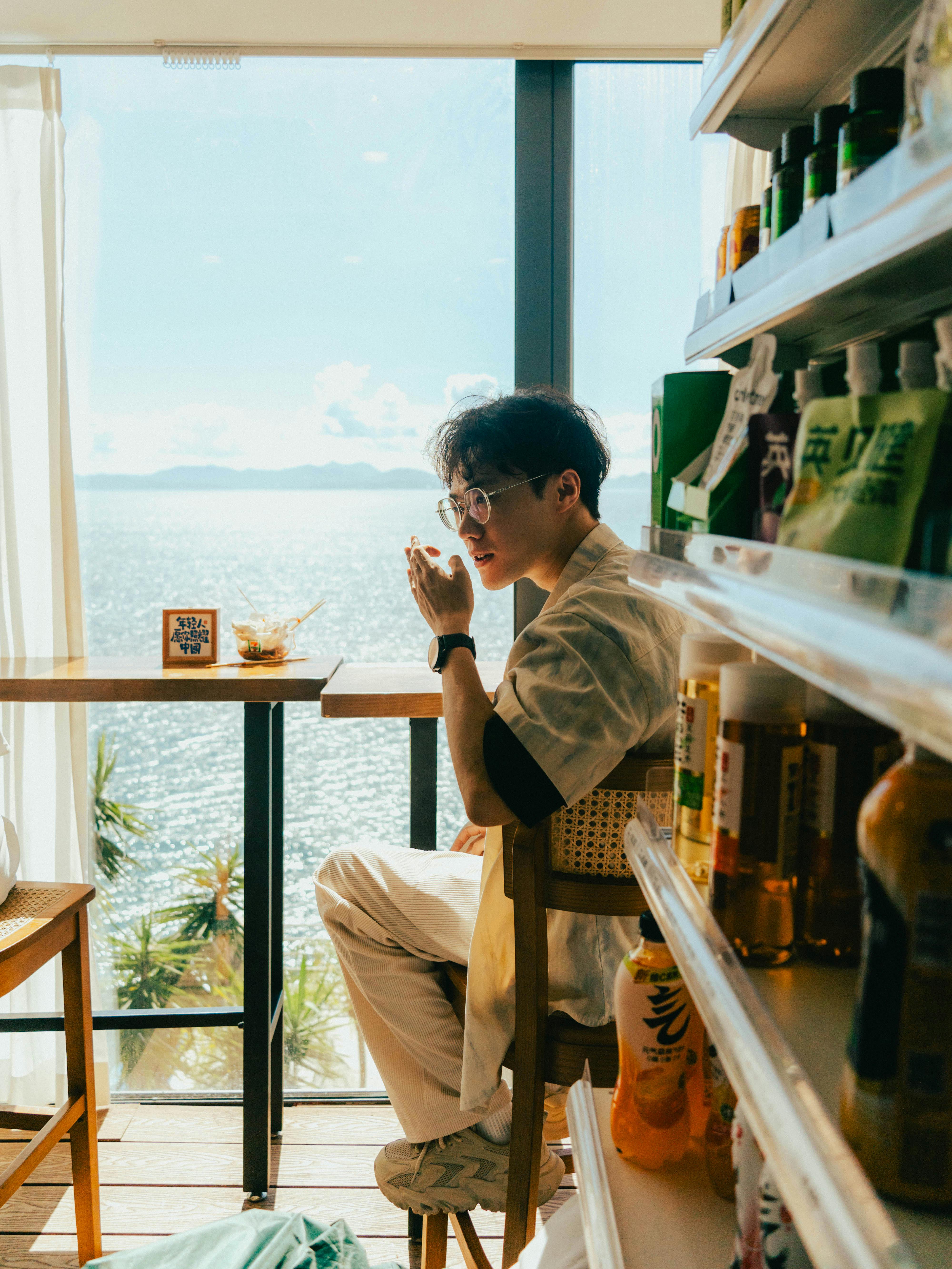 一名男子在海边的窗户旁喝着饮料，欣赏着美丽的海景