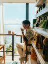 一名男子在海边的窗户旁喝着饮料，欣赏着美丽的海景