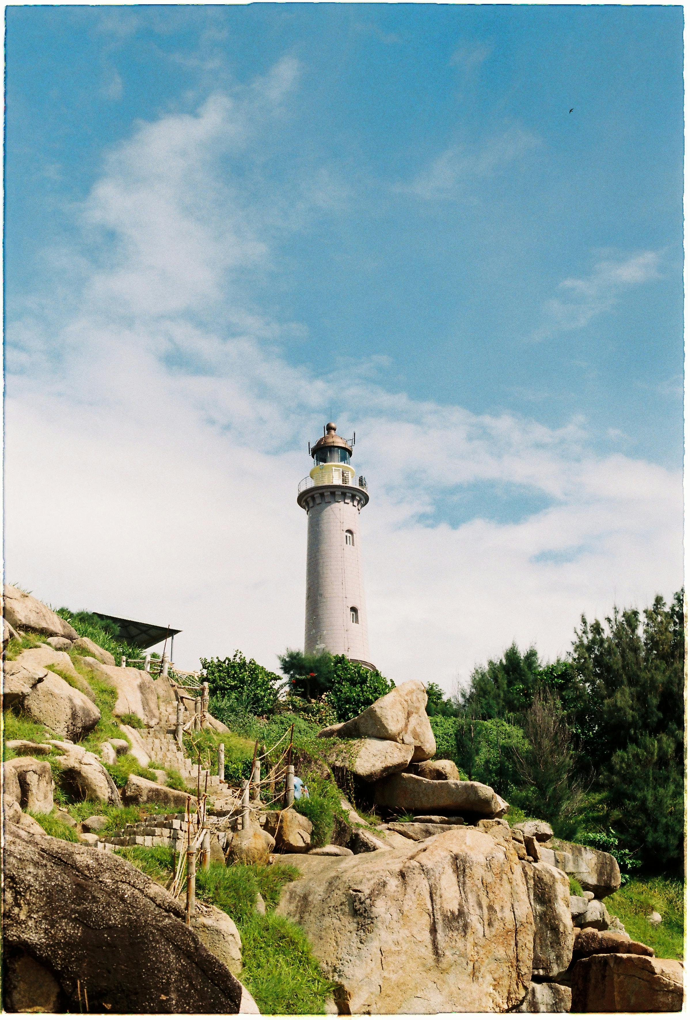 高耸的灯塔背靠着充满活力的蓝天，周围环绕着天然岩石地形