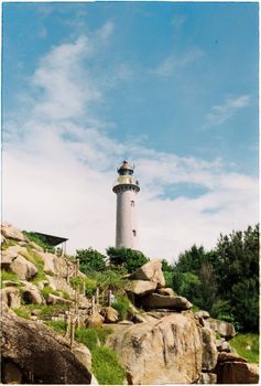 高耸的灯塔背靠着充满活力的蓝天，周围环绕着天然岩石地形