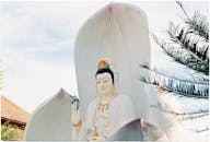 一尊宁静的佛像，周围绿树成荫，天空晴朗，散发着宁静