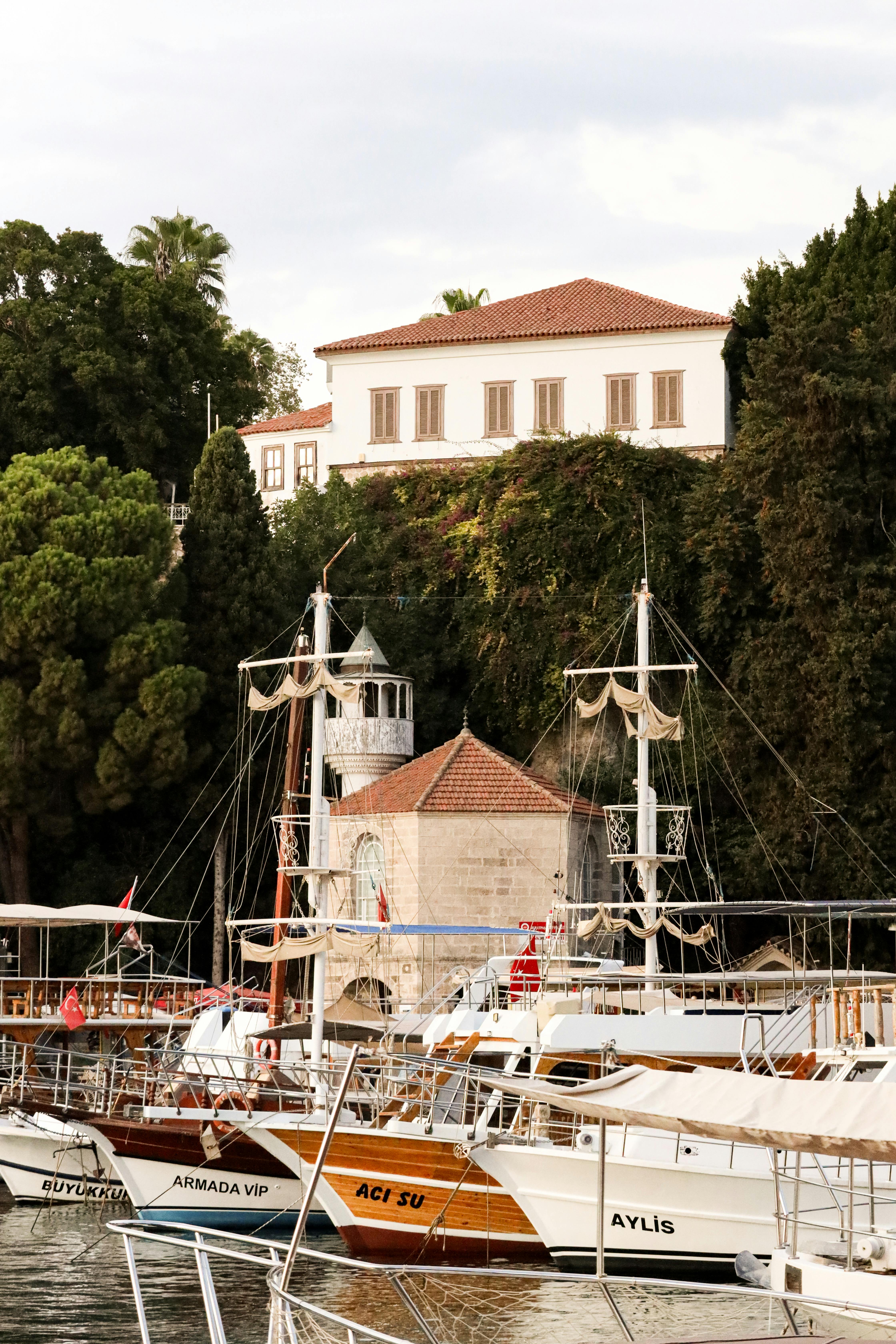 一个宁静的海港景象，帆船停靠在一座被树木环绕的历史建筑前