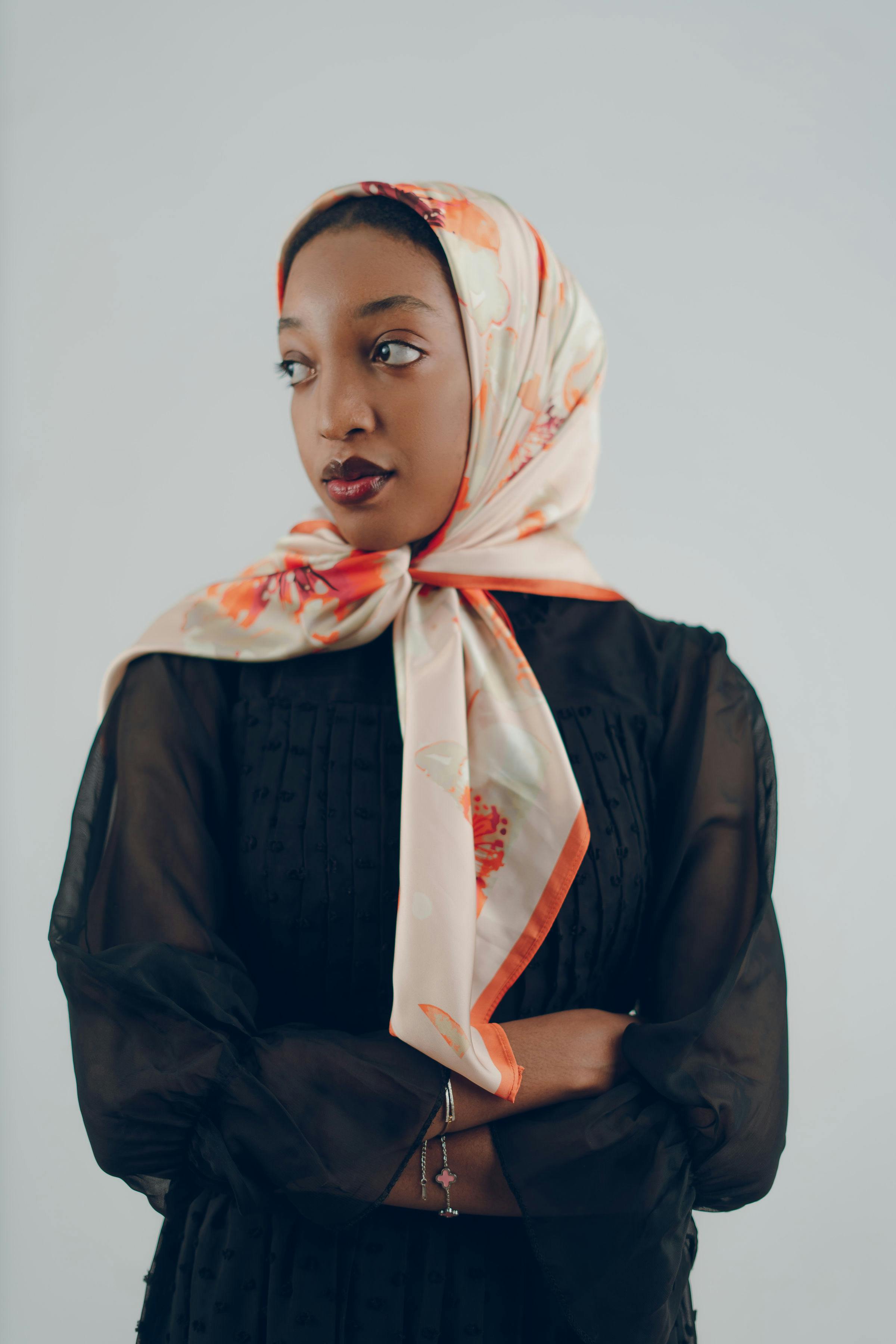 一位优雅的女士，头戴花卉图案的头巾，身着黑色薄纱连衣裙，自信地看向一旁