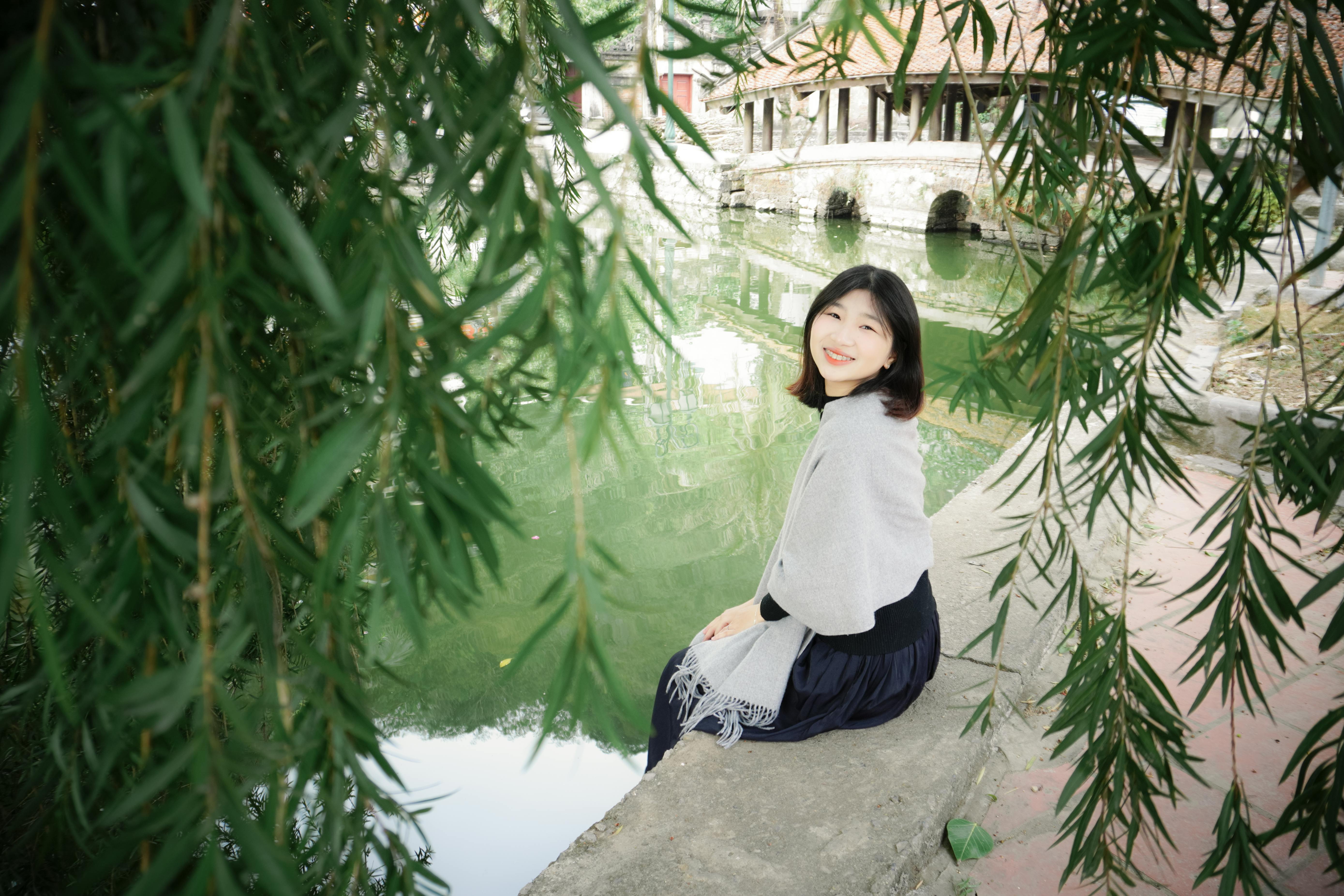 一位年轻女子坐在河内一个宁静的湖边，周围郁郁葱葱，表达着和平