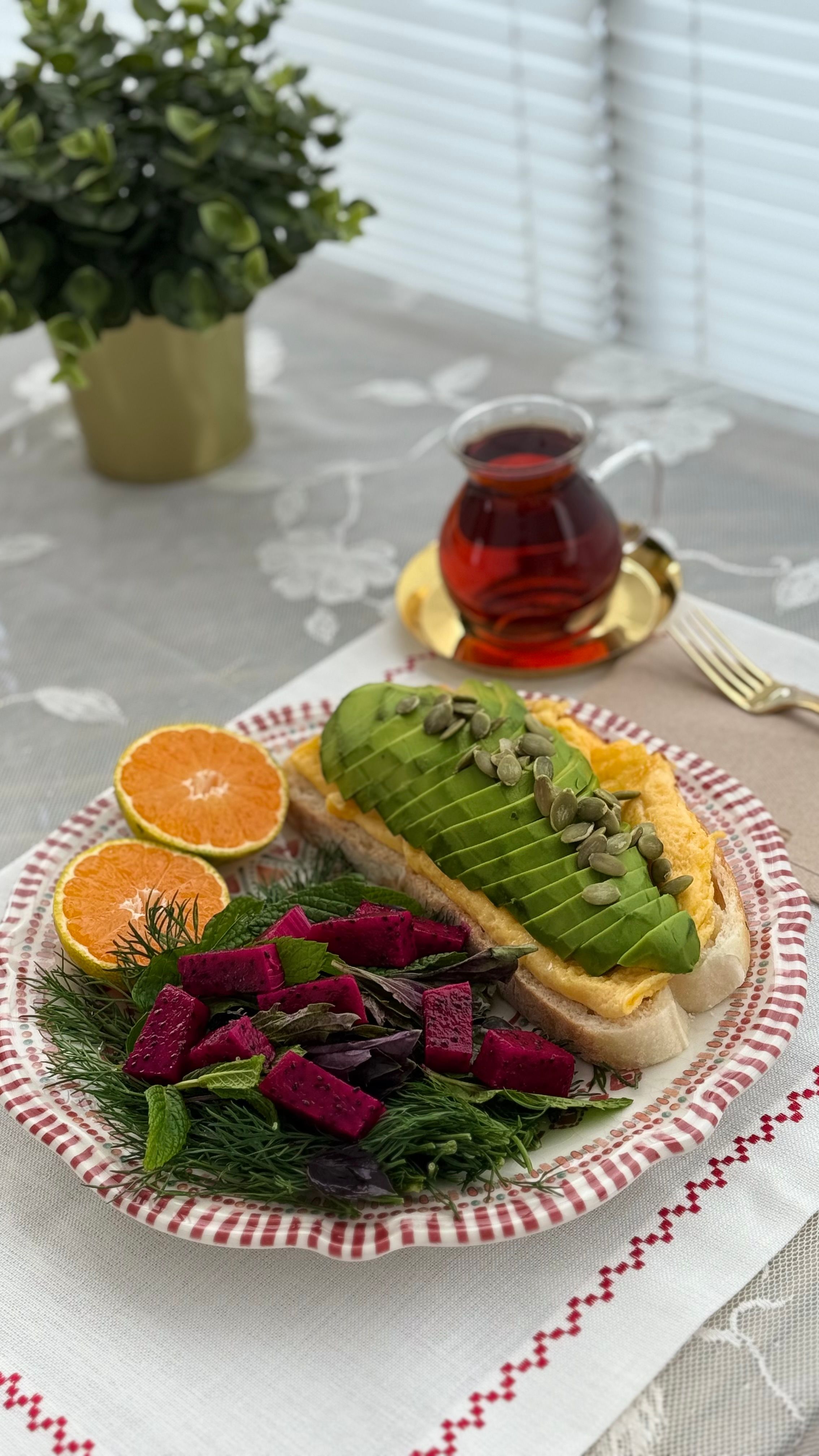 Plate of avocado toast with tea, oranges, and salad on a table.