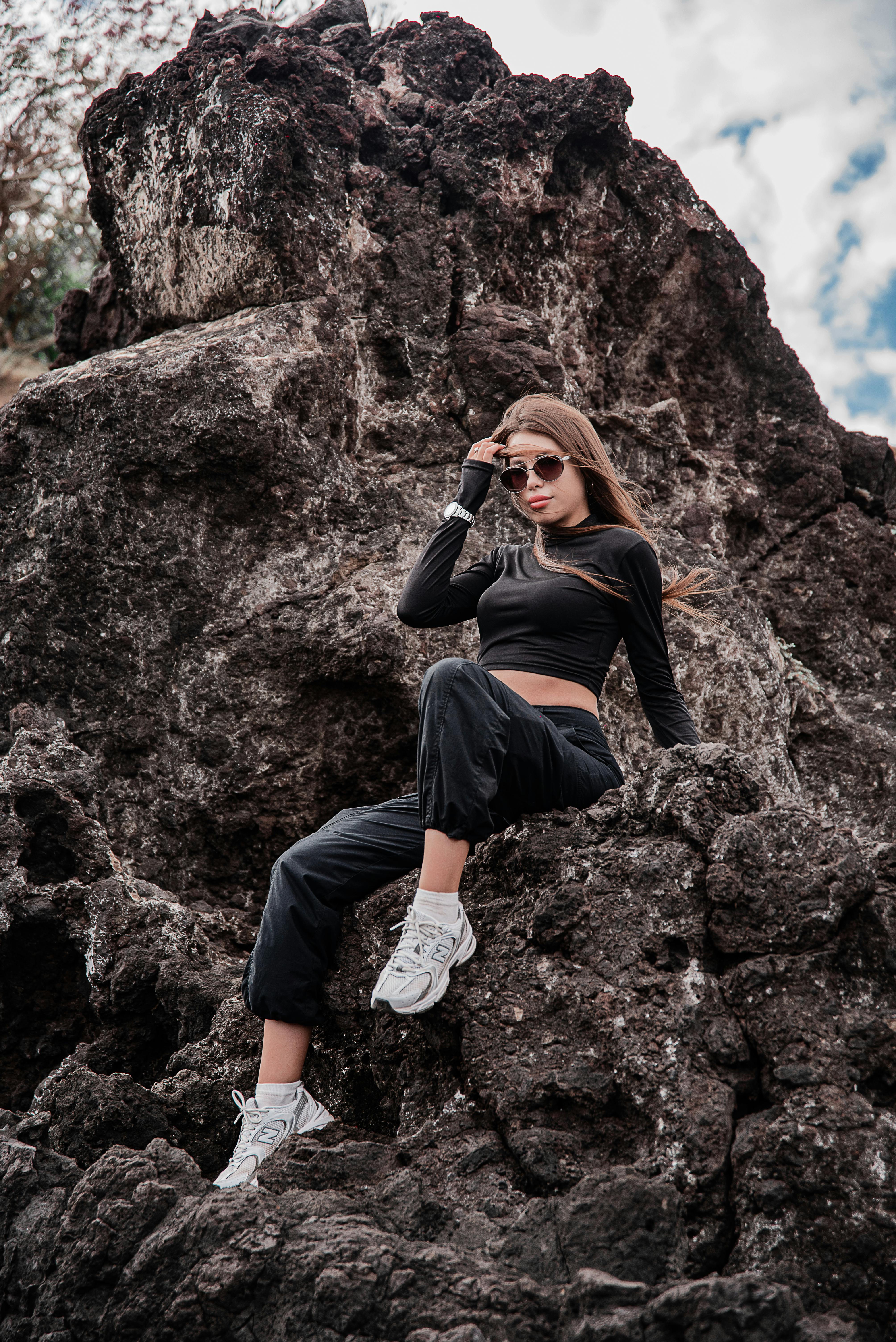 在明亮的天空下，一名身着时尚服装的女子自信地在岩石上摆姿势