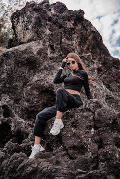 在明亮的天空下，一名身着时尚服装的女子自信地在岩石上摆姿势