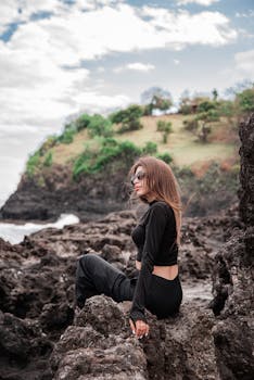 黑衣女子坐在风景优美的岩石岸边，享受着海边平静的一天