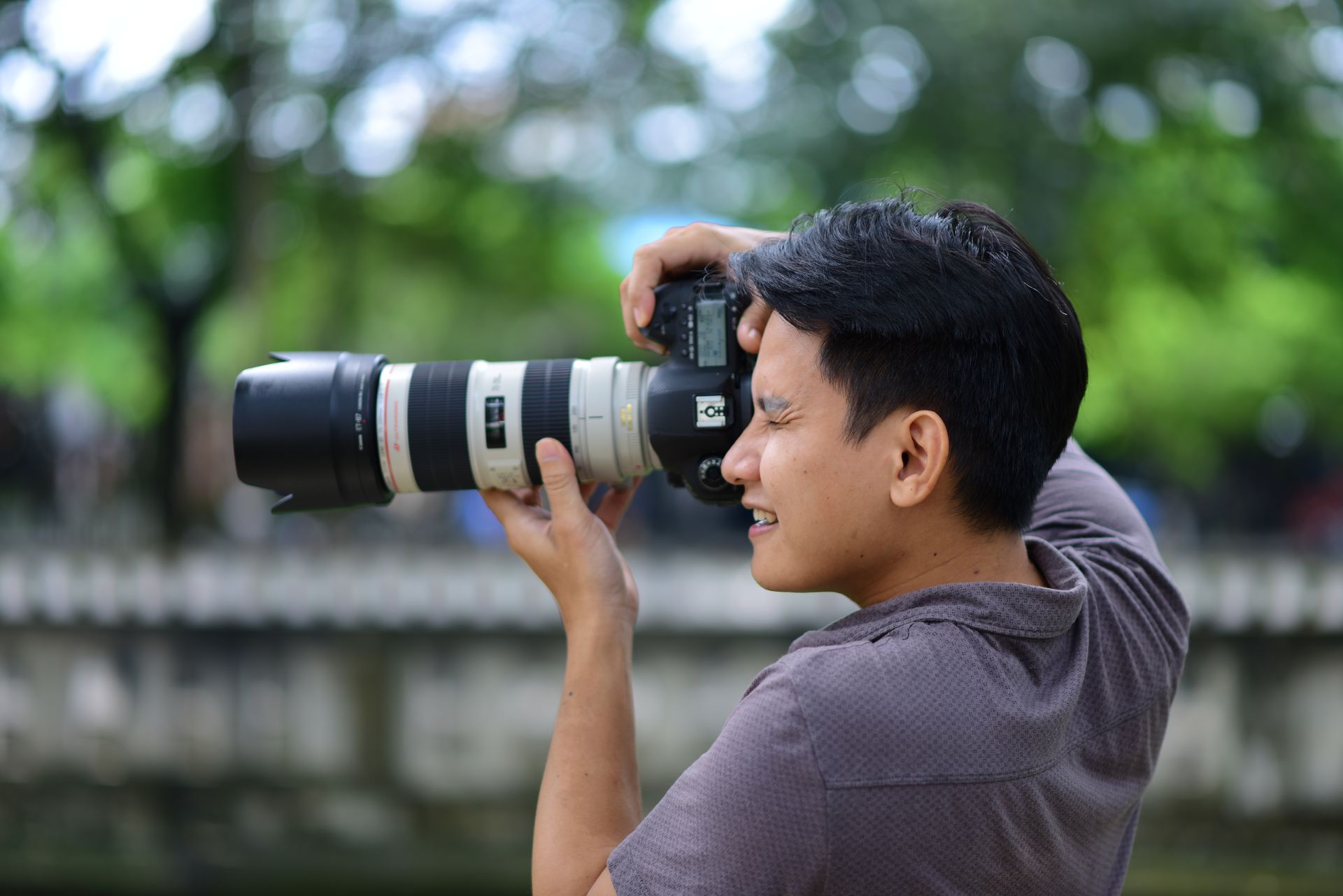 A focused photographer using a DSLR camera with a large lens outdoors against a green backdrop.