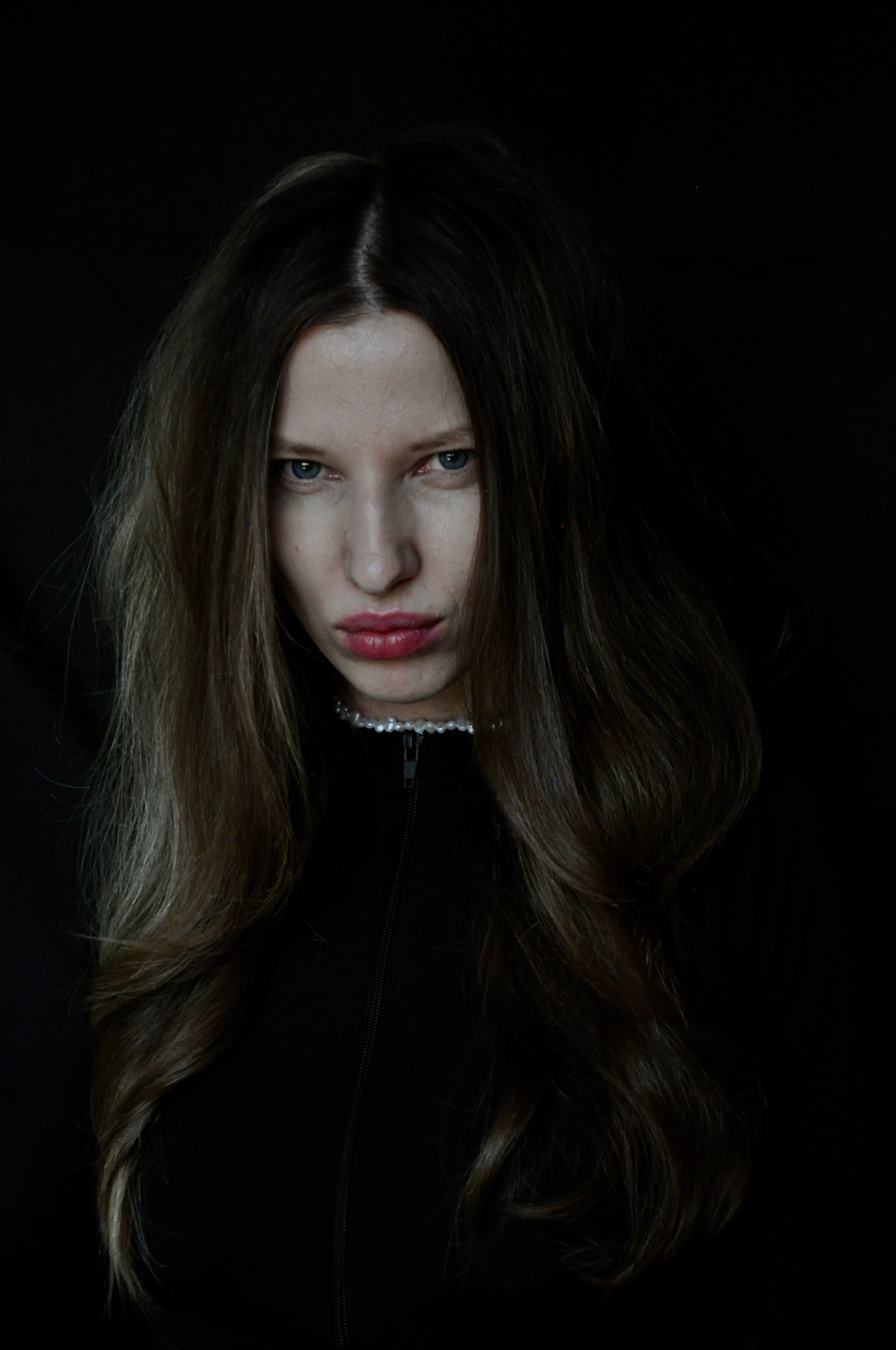 A striking portrait of a woman with dark hair against a black background, conveying mystery and intensity.