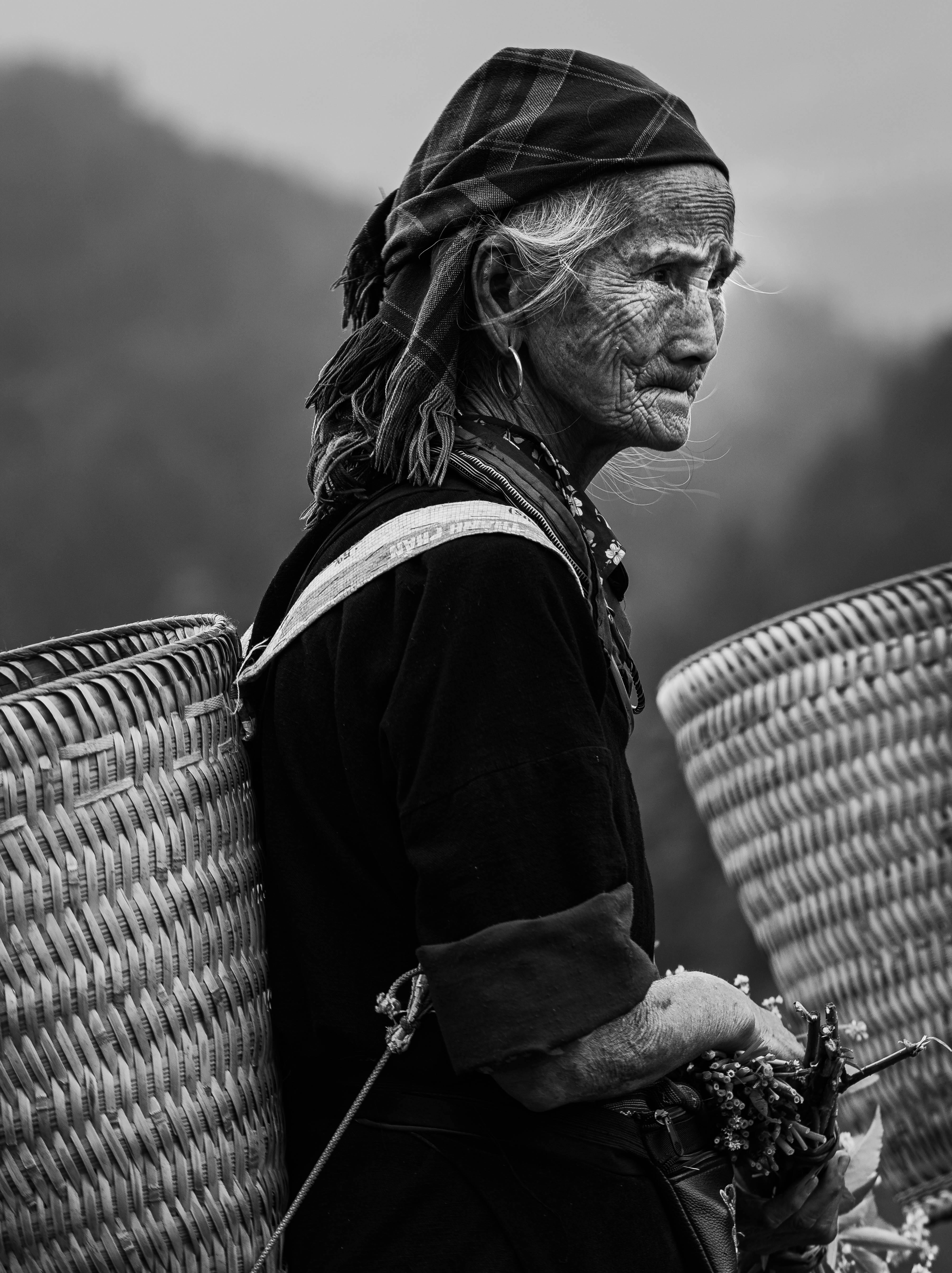 Elderly woman in traditional ethnic dress and baskets, black and white portrait.