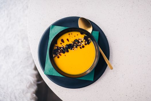 Top view of creamy pumpkin soup with seeds and sauce on a white table.