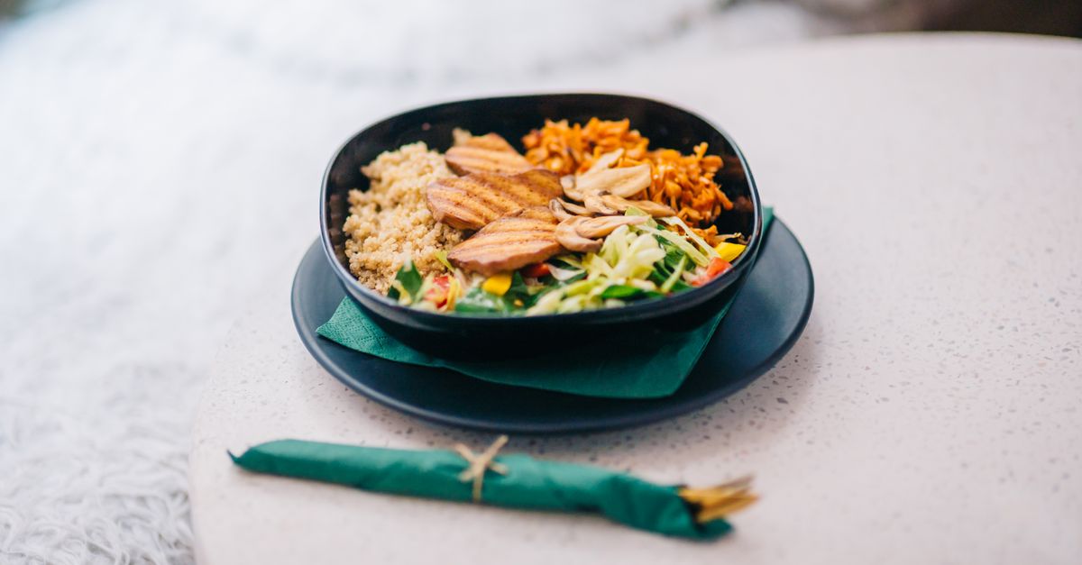 Colorful quinoa bowl with grilled salmon, avocado slices, and fresh herbs on a rustic wooden table