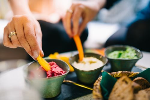 Free A person dipping vegetables into vibrant dips at an indoor gathering. Stock Photo