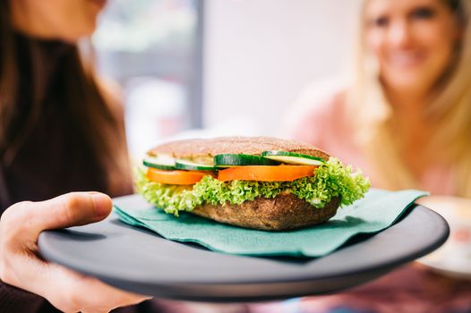 Close-up of a fresh vegetable sandwich held on a black tray by diners.