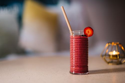 Free Red strawberry smoothie in a ribbed glass with a paper straw and candlelit atmosphere. Stock Photo