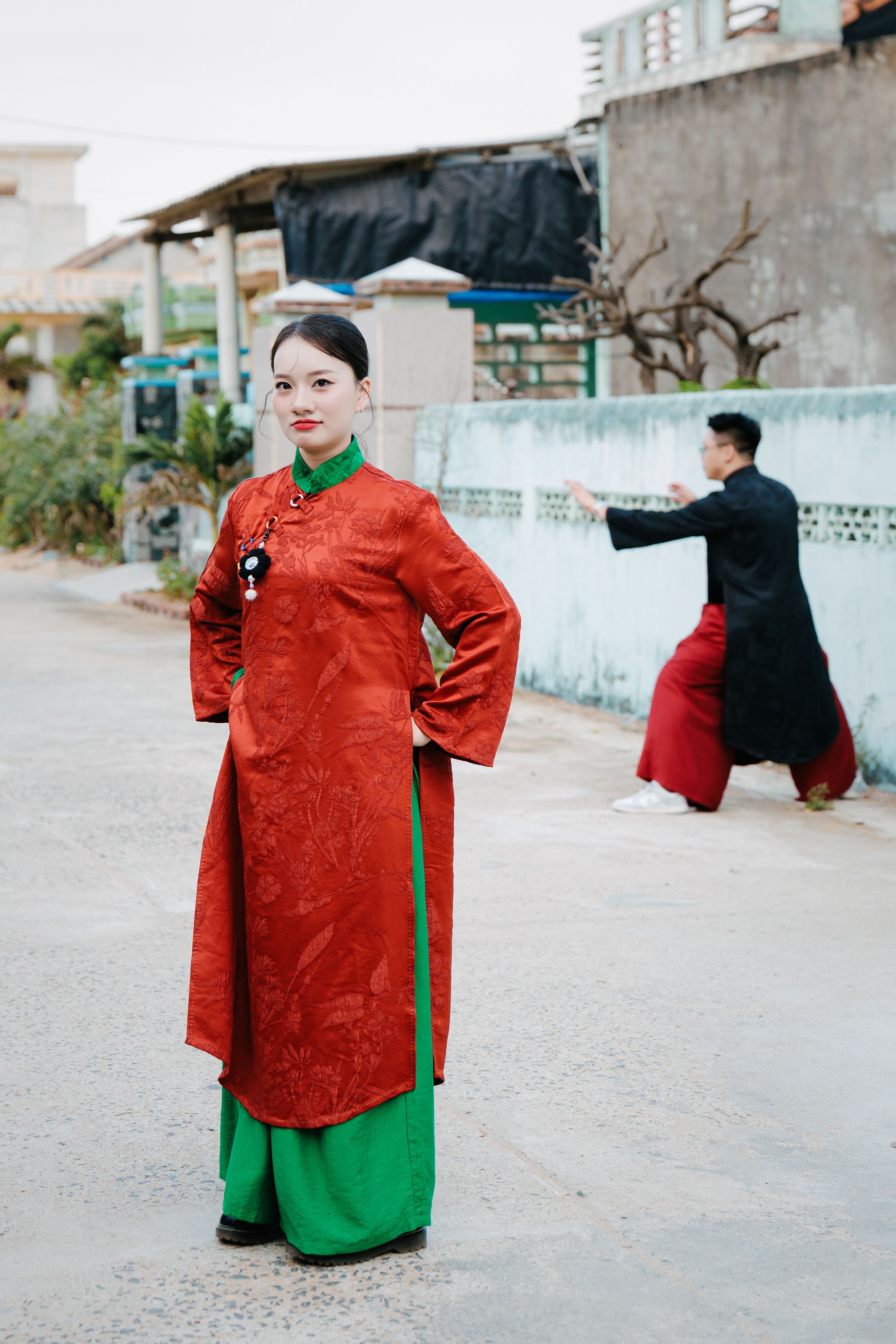 Elegant portrait of a woman in Vietnamese áo dài with traditional red and green attire outdoors.