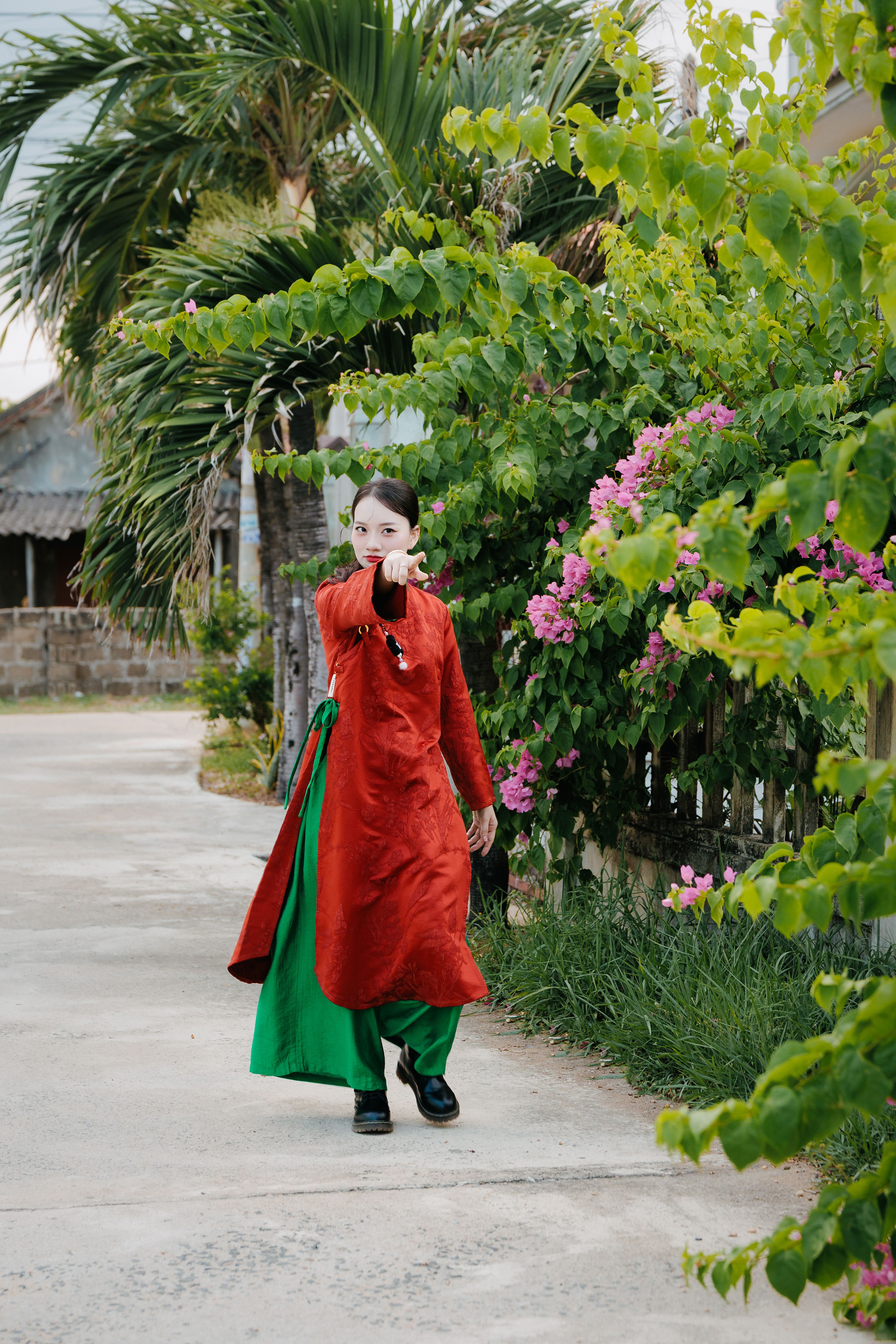 A young woman in a vibrant traditional outfit walking along a lush pathway lined with tropical plants.
