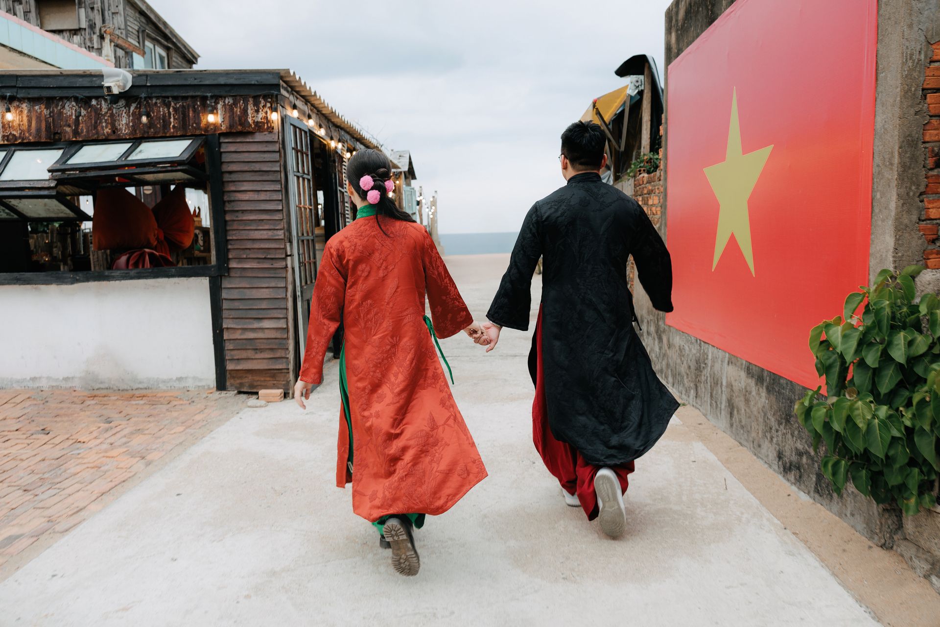 Couple dressed in Vietnamese traditional clothing walking hand in hand by a Vietnamese flag.