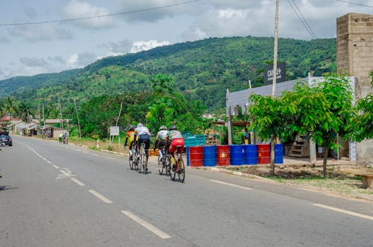Group of cyclists racing on a tranquil road surrounded by lush green hills and trees.