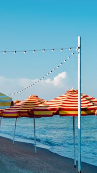 Vibrant striped umbrellas on a sunny beach with calming waves and clear blue sky.