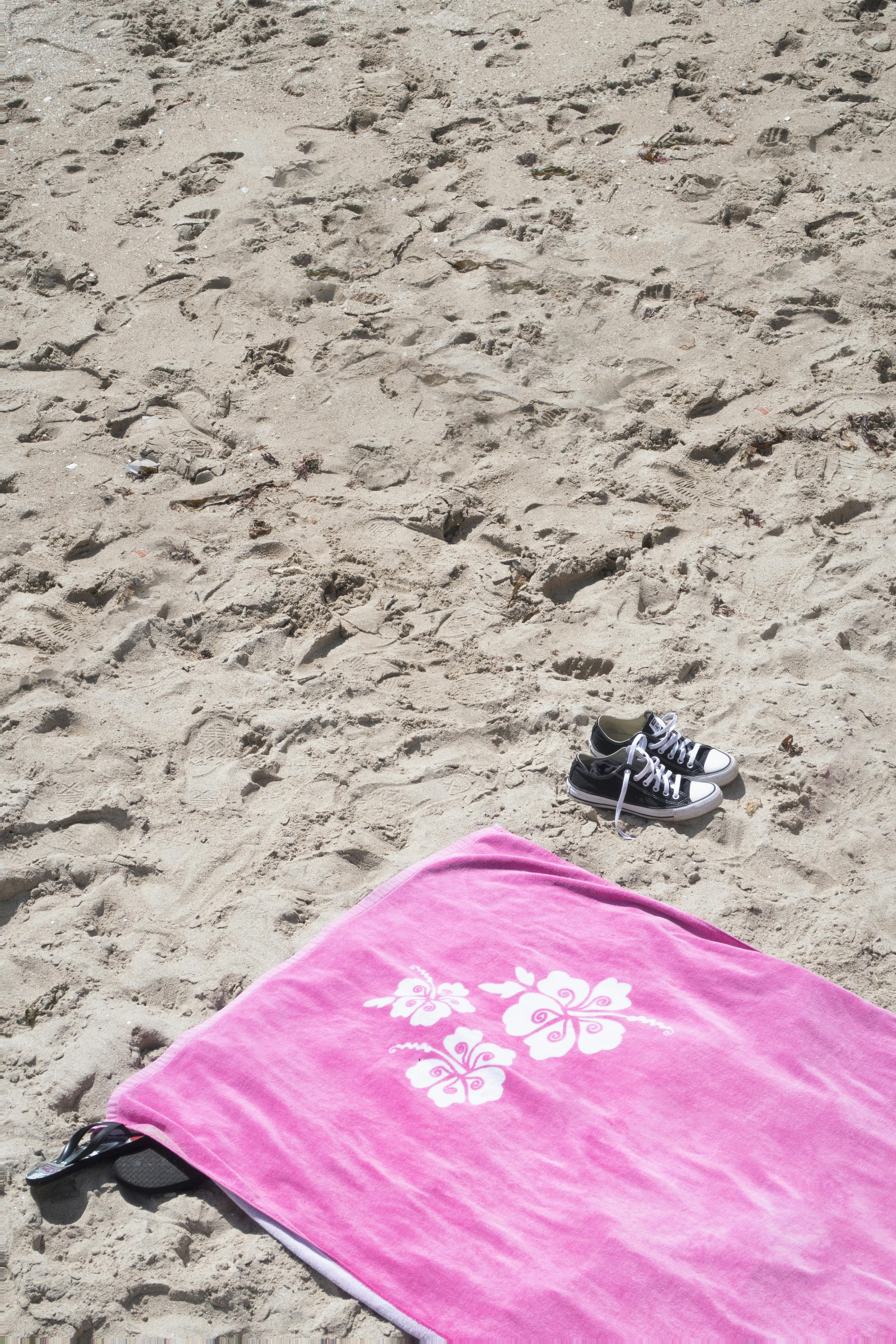 明亮的粉红色沙滩巾和运动鞋在沙滩上唤起了夏季的休闲和放松
