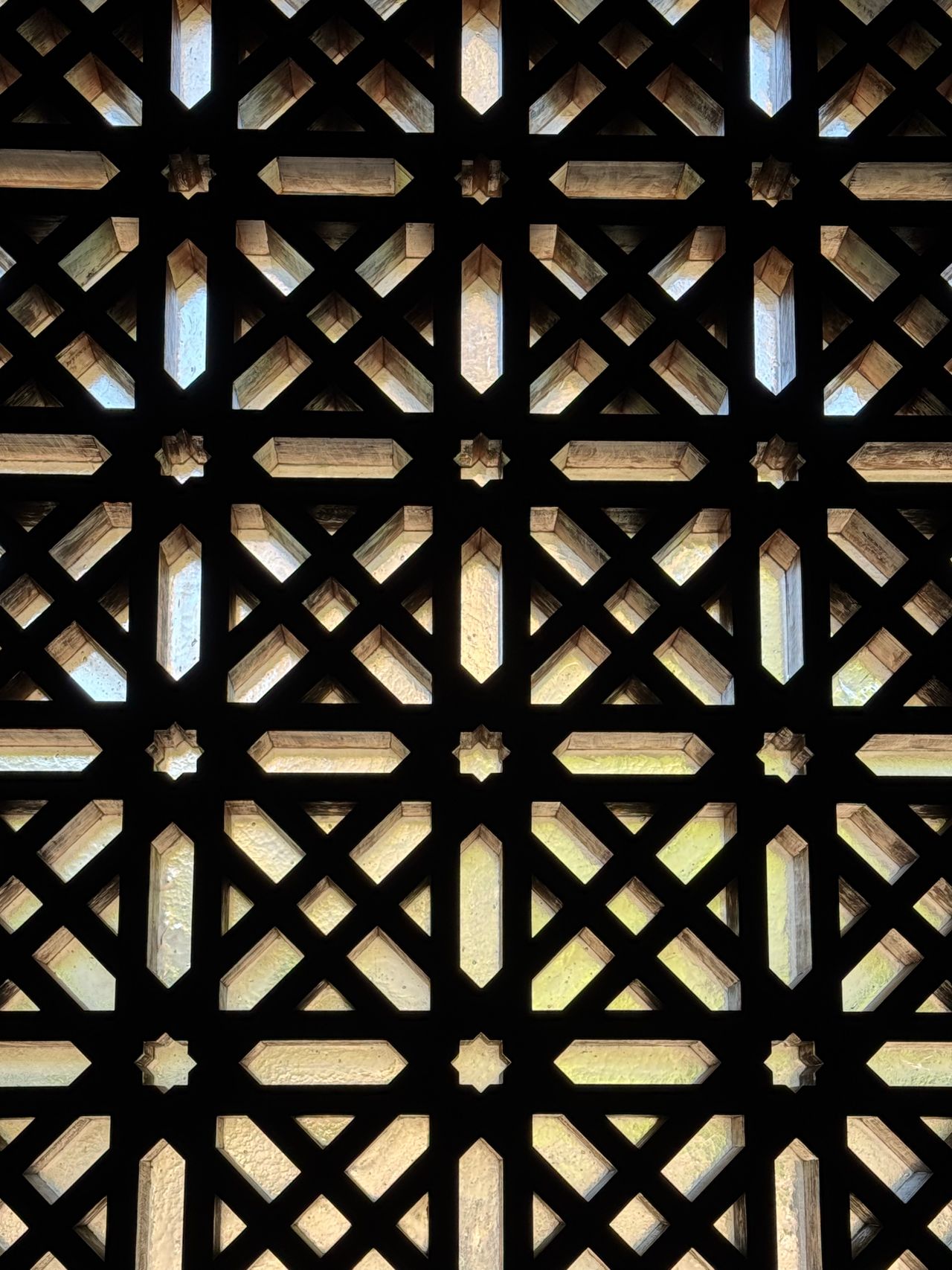Close-up of a dark geometric lattice screen with sunlight filtering through
