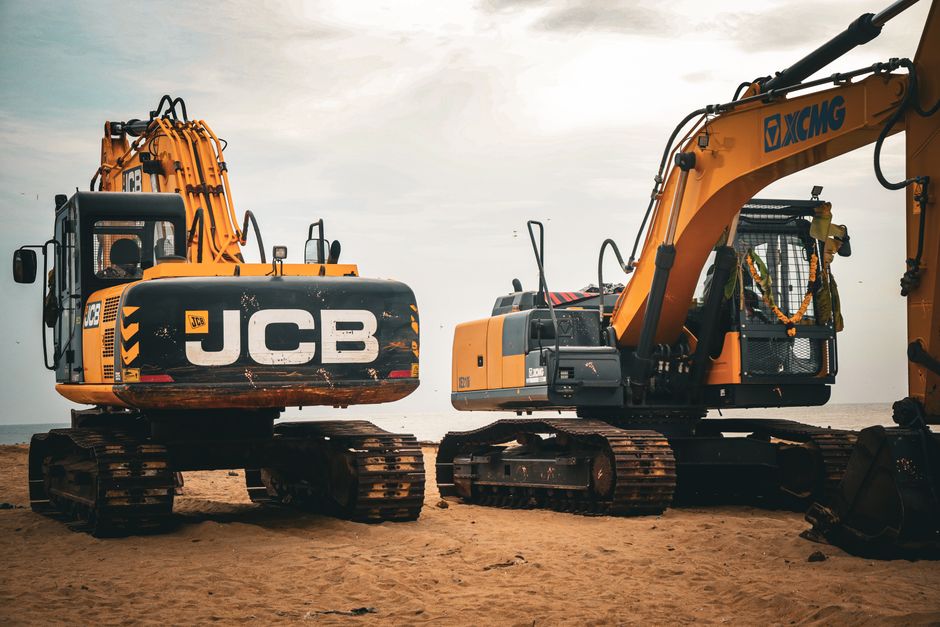 Two heavy excavators on a sandy beach, showcasing industrial construction machinery.