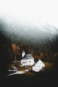 Scenic view of a quaint church surrounded by misty forests in Austria's fall setting.