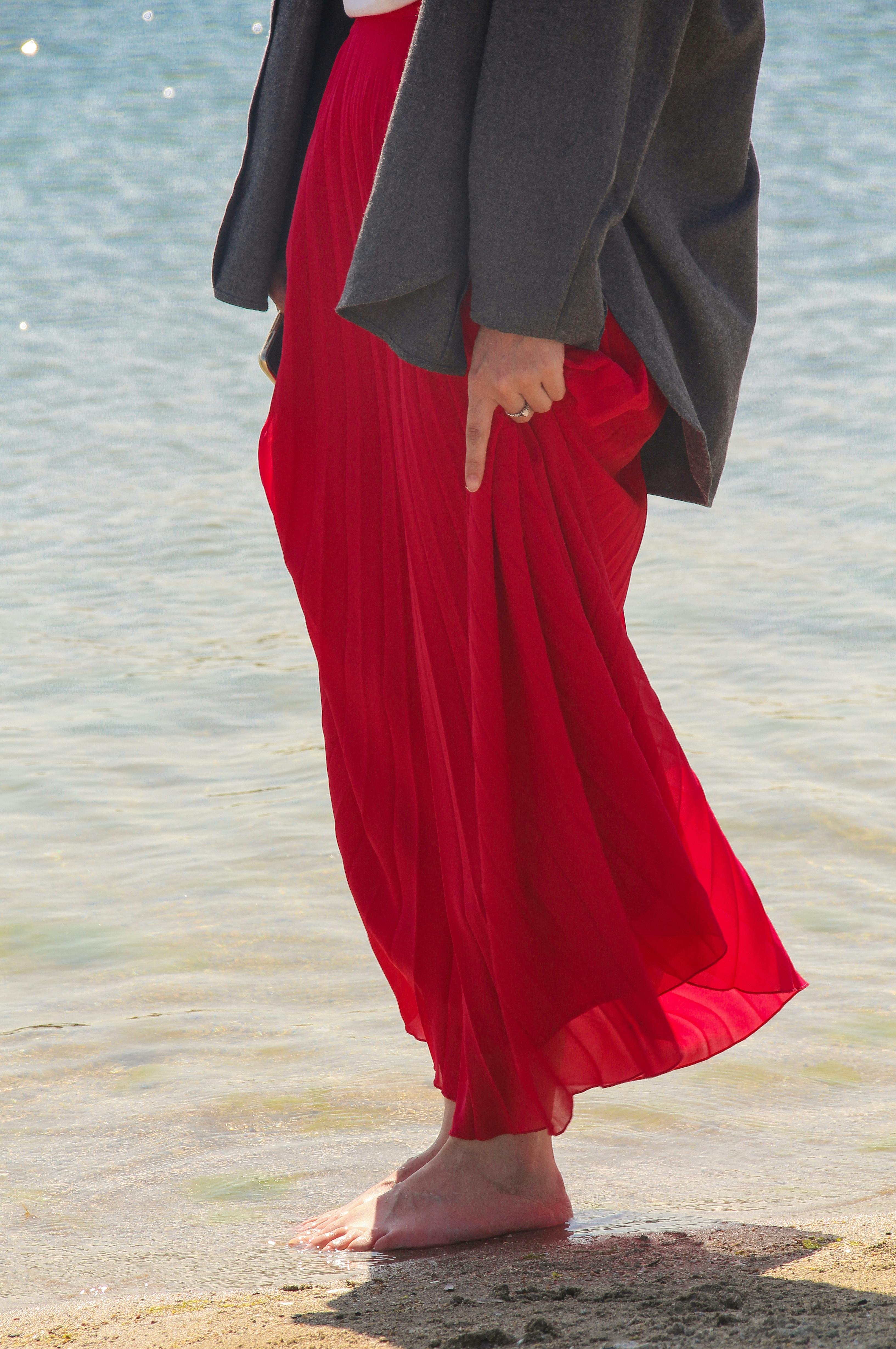 穿着红色裙子的女人赤脚站在海边，捕捉到宁静与自由