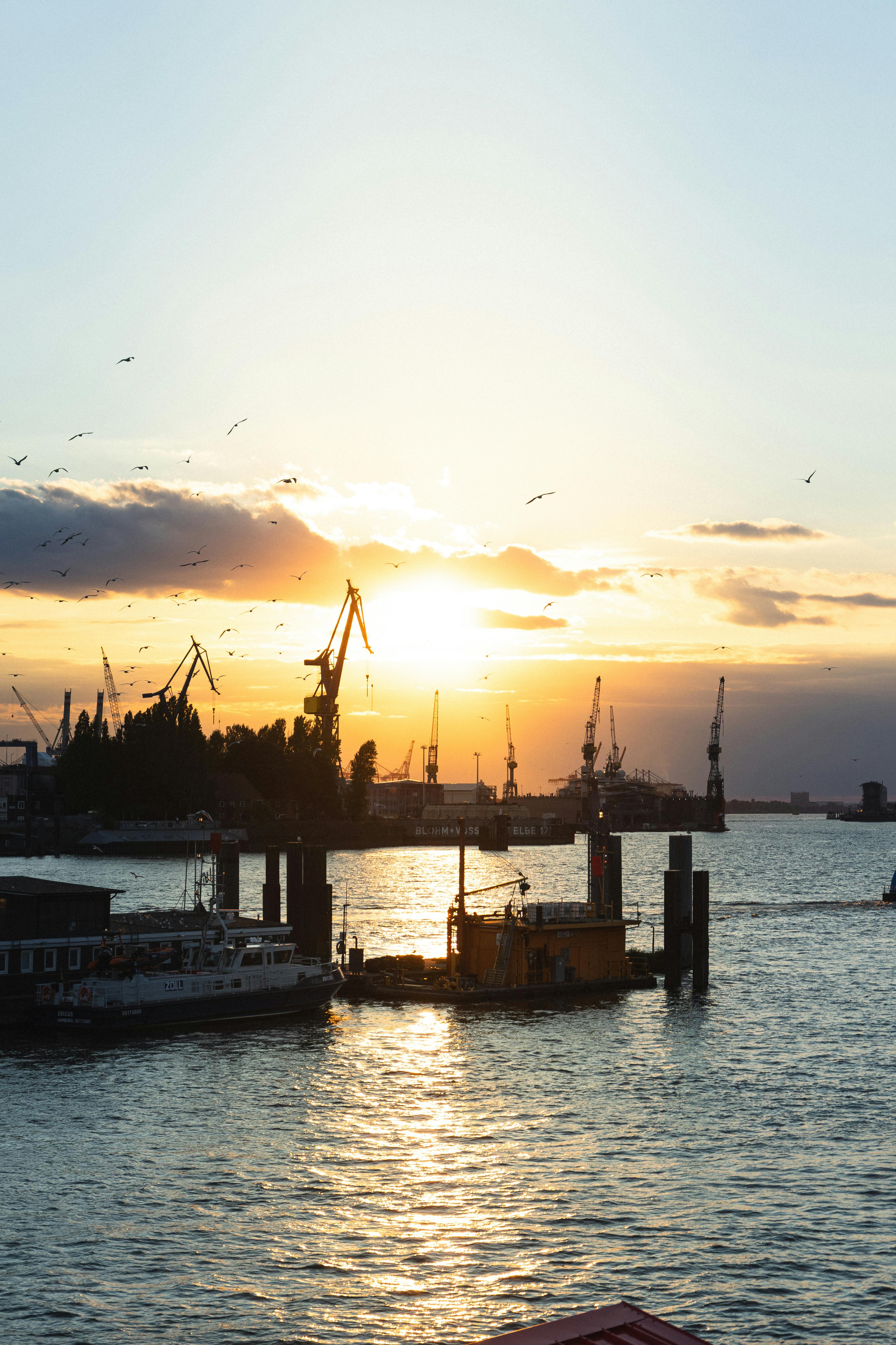 在工业港口上空，迷人的日落映照天际，起重机的剪影在天空中若隐若现