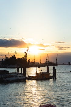 在工业港口上空，迷人的日落映照天际，起重机的剪影在天空中若隐若现