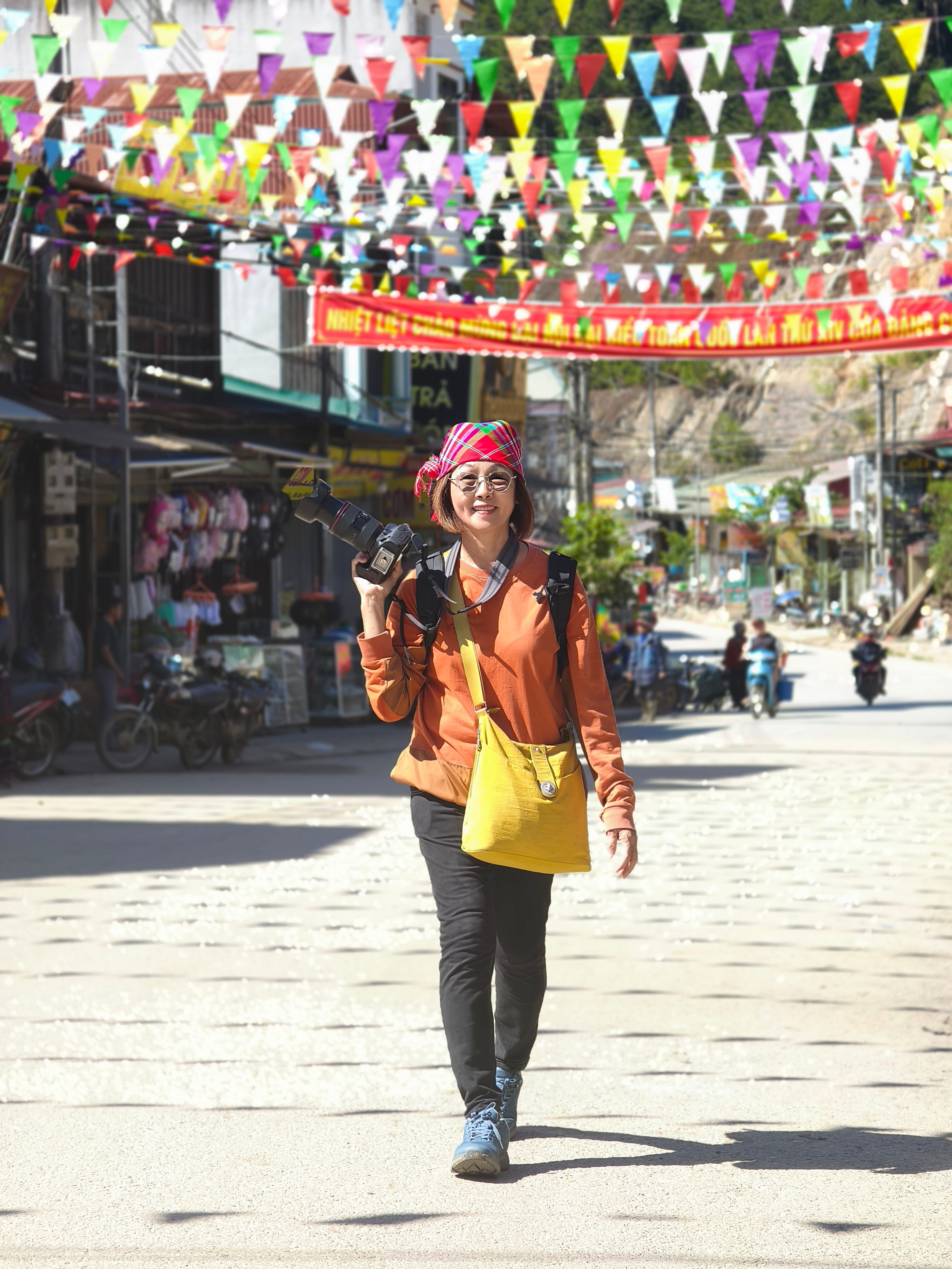Woman with camera walks under colorful festival flags in vibrant street.