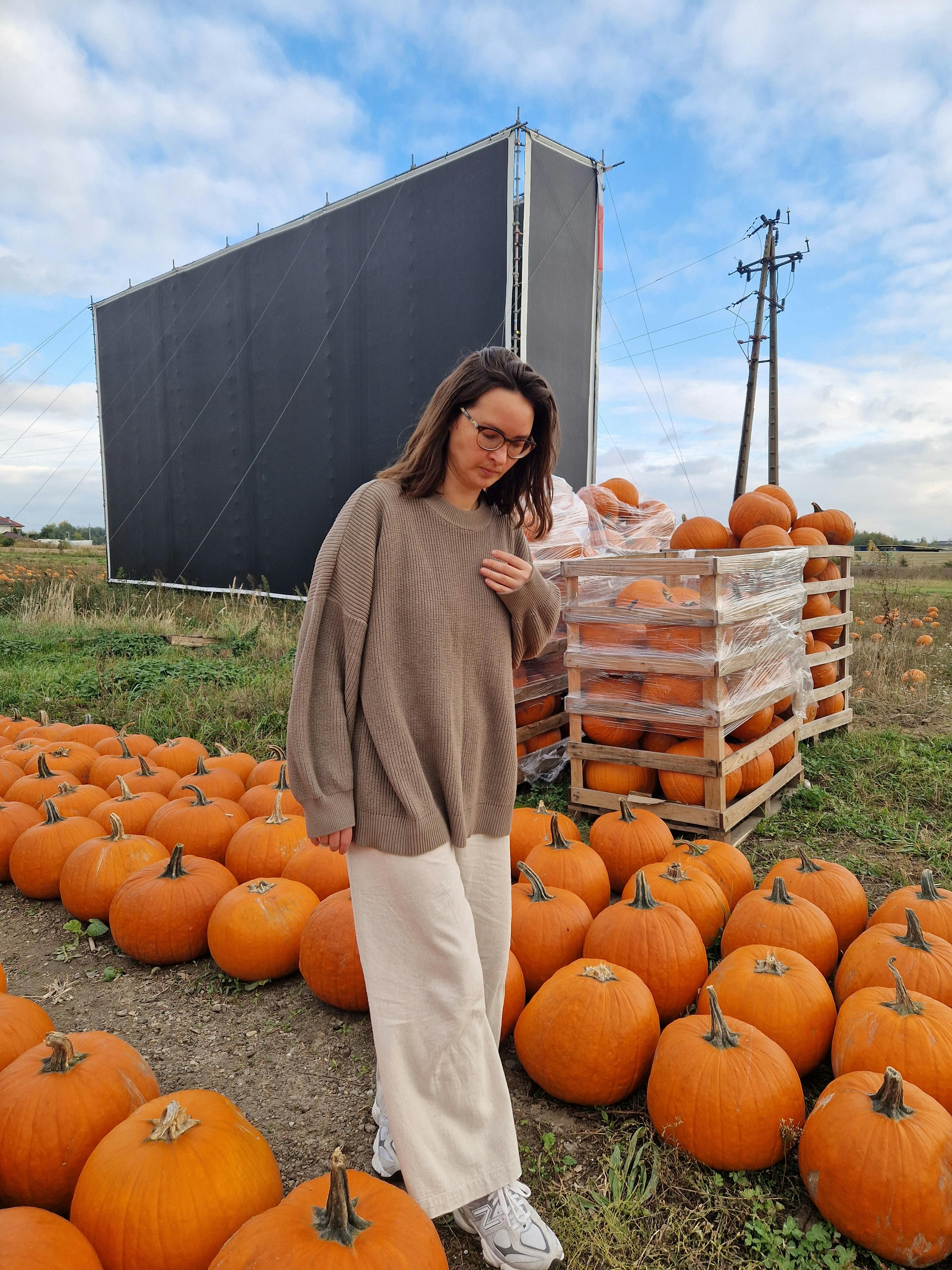 穿着舒适毛衣的女人站在户外，周围是秋天的南瓜